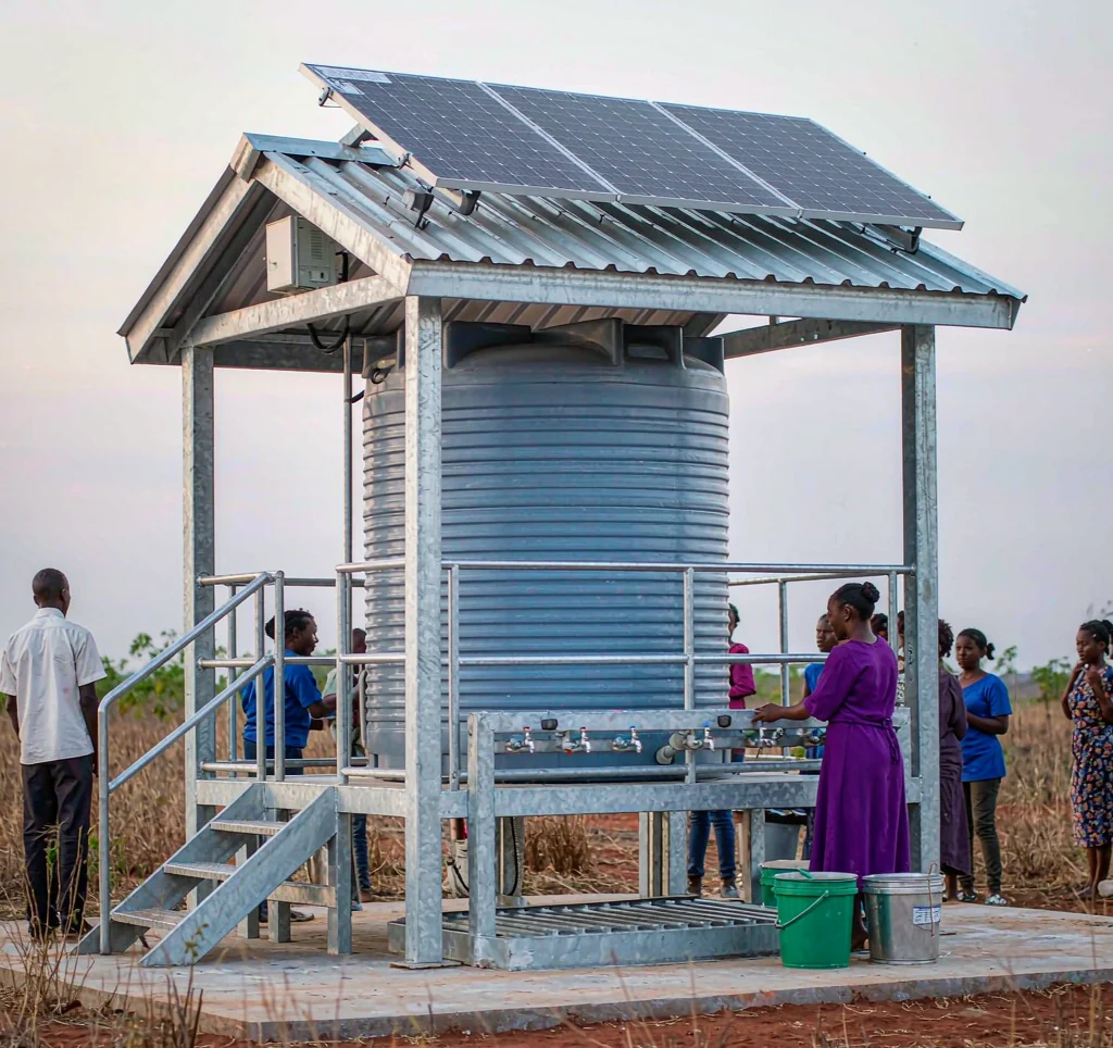 Solar powered water kiosk in an African community with solar panels, storage tank and people collecting water
